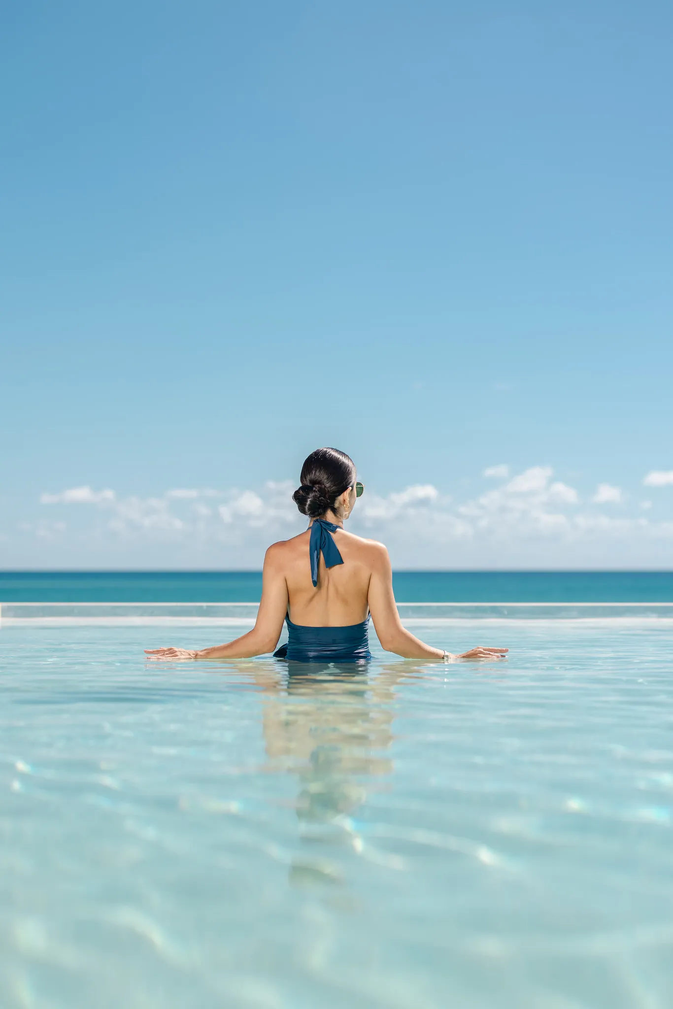 Woman relaxing in an infinity pool overlooking the Caribbean Sea at Secrets Mirabel Cancun Resort & Spa.