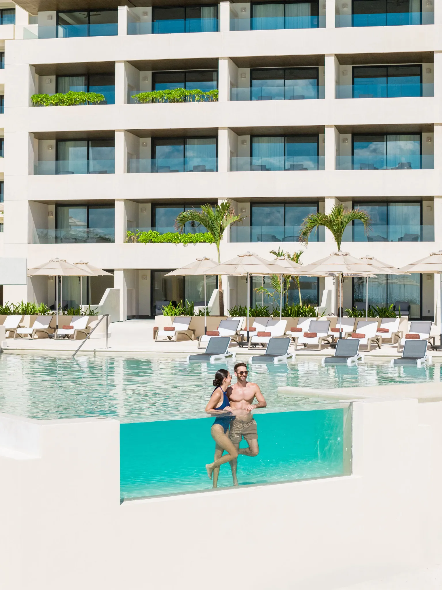 Couple relaxing in the main pool at Secrets Mirabel Cancun Resort & Spa with luxury accommodations in the background.